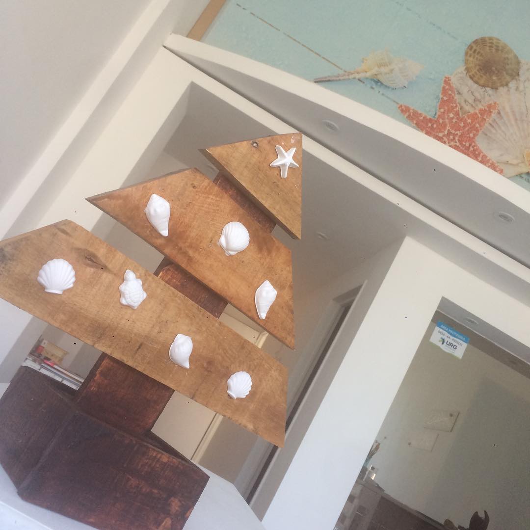 Un arbolito de madera decorado con caracolas blancas, bajo el panel turquesa con estrellas de mar y caracolas del spa